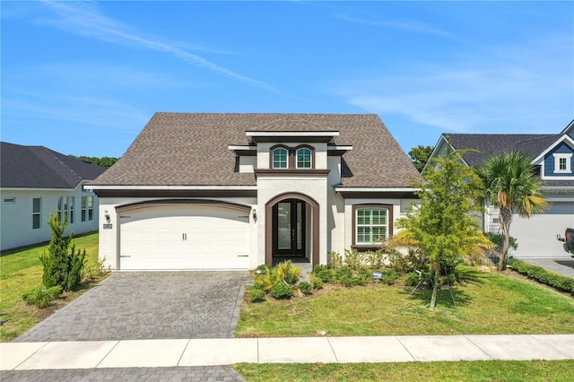 traditional home with roof with shingles, a garage, decorative driveway, a front lawn, and stucco siding