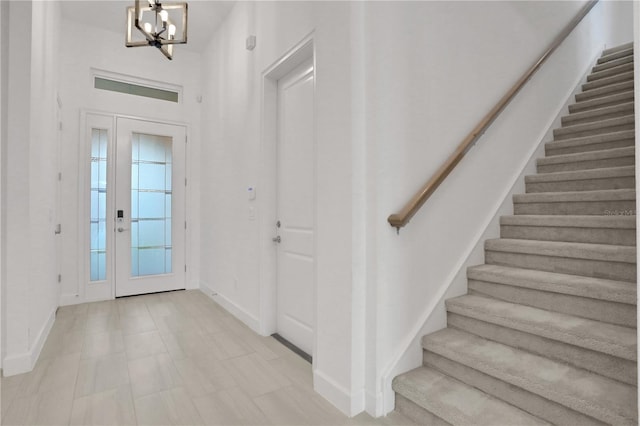 foyer entrance featuring baseboards, stairs, a notable chandelier, and a wealth of natural light