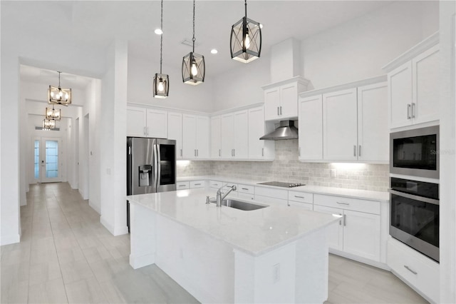 kitchen with wall chimney range hood, appliances with stainless steel finishes, tasteful backsplash, a sink, and white cabinets