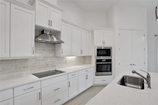 kitchen with oven, wall chimney exhaust hood, black electric cooktop, built in microwave, and a sink
