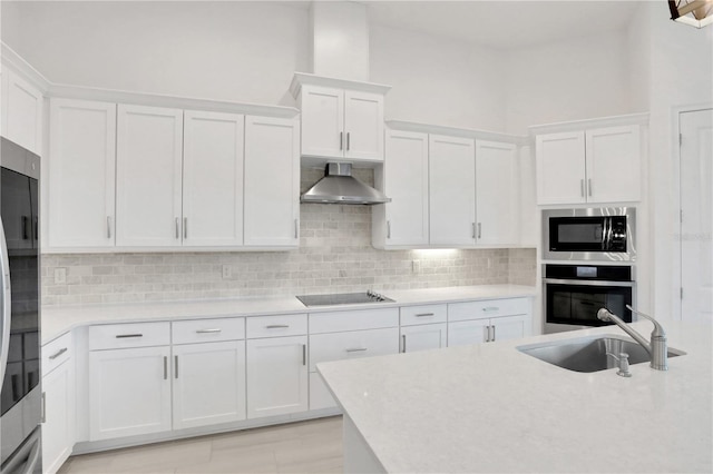 kitchen featuring light countertops, wall chimney exhaust hood, white cabinetry, a sink, and appliances with stainless steel finishes