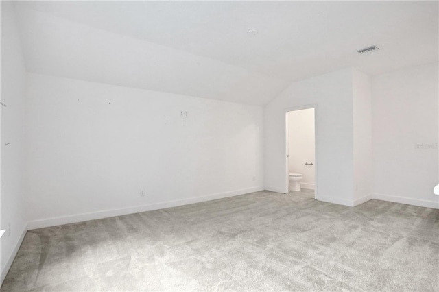 empty room with light colored carpet, baseboards, visible vents, and vaulted ceiling