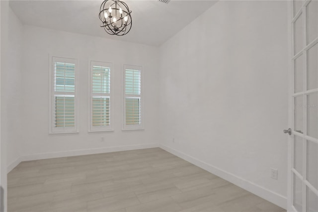 empty room with baseboards, a notable chandelier, and light wood-type flooring