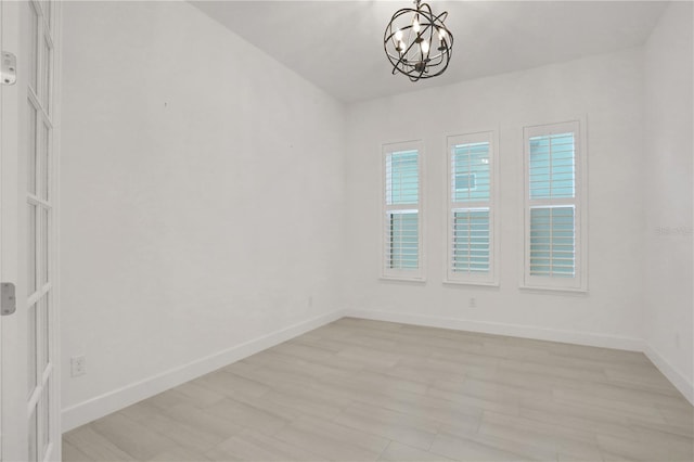 spare room with baseboards, a chandelier, and light wood-style floors