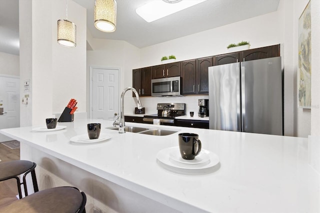 kitchen with a breakfast bar, a sink, stainless steel appliances, dark brown cabinetry, and hanging light fixtures