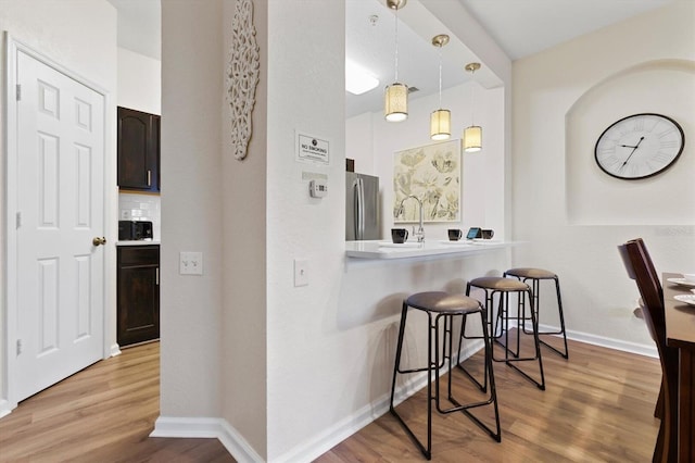 kitchen with a kitchen breakfast bar, light wood-style flooring, tasteful backsplash, and freestanding refrigerator