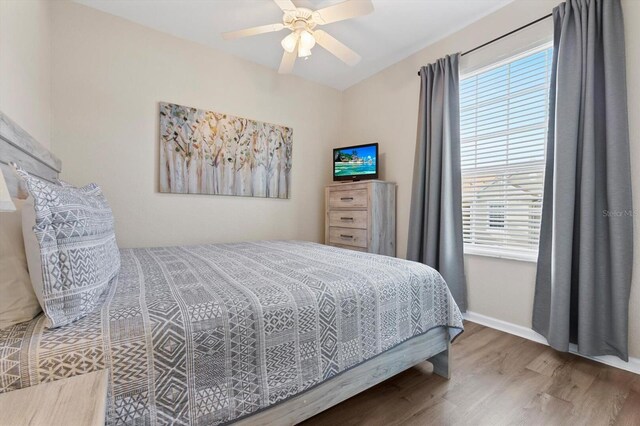 bedroom featuring multiple windows, a ceiling fan, baseboards, and wood finished floors