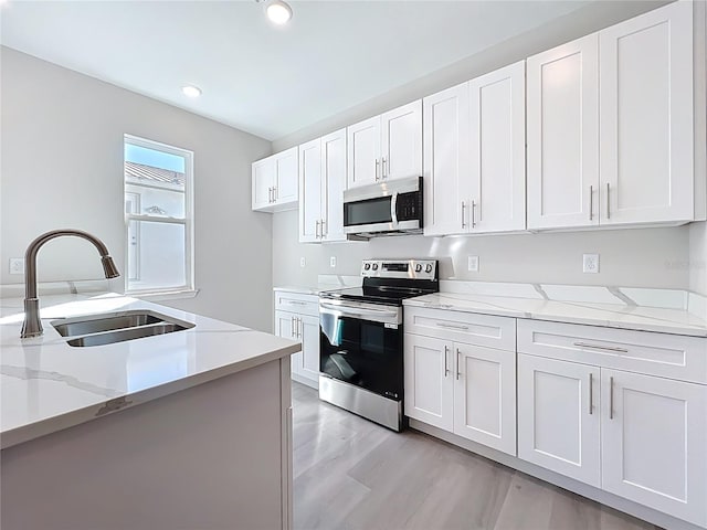 kitchen with a sink, white cabinets, light stone counters, and stainless steel appliances