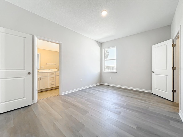 unfurnished bedroom featuring baseboards, a textured ceiling, light wood-style flooring, and ensuite bathroom