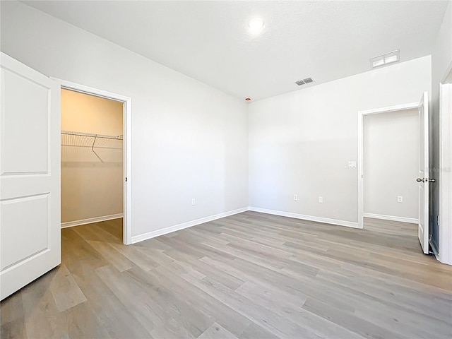 unfurnished bedroom featuring visible vents, baseboards, a spacious closet, and light wood finished floors