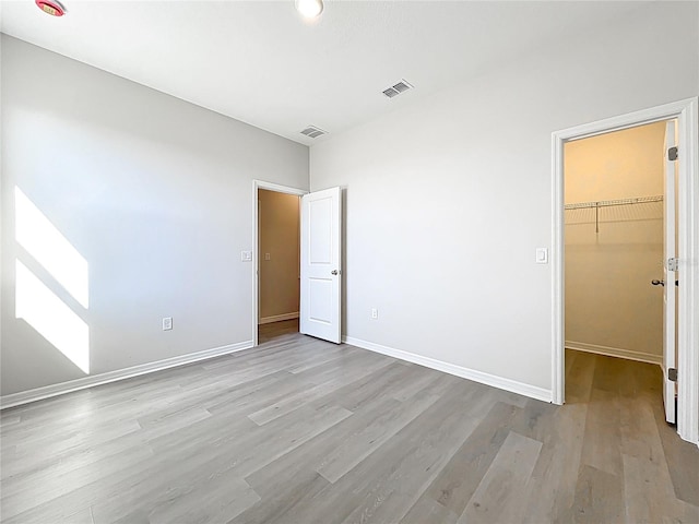 unfurnished bedroom featuring visible vents, baseboards, a spacious closet, and light wood finished floors