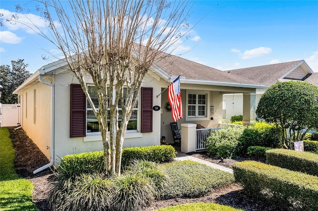 bungalow-style house with stucco siding, covered porch, roof with shingles, and fence