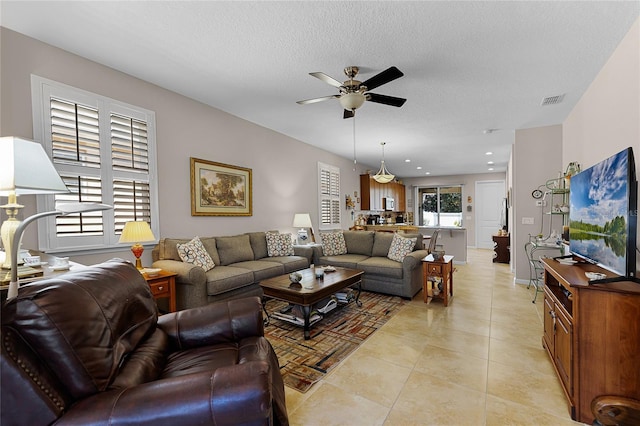 living room with light tile patterned floors, a ceiling fan, visible vents, and a textured ceiling