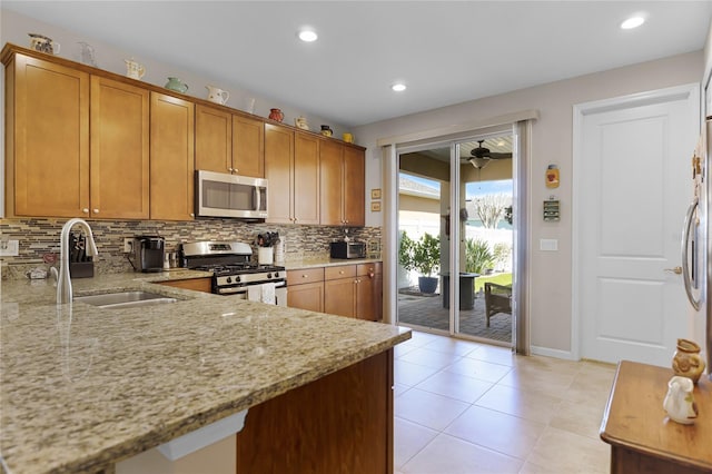 kitchen featuring backsplash, light stone counters, appliances with stainless steel finishes, brown cabinetry, and a sink