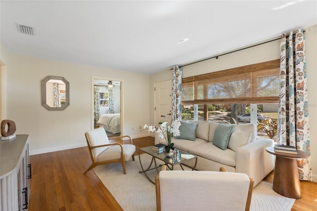 living area with visible vents, a ceiling fan, baseboards, and wood finished floors