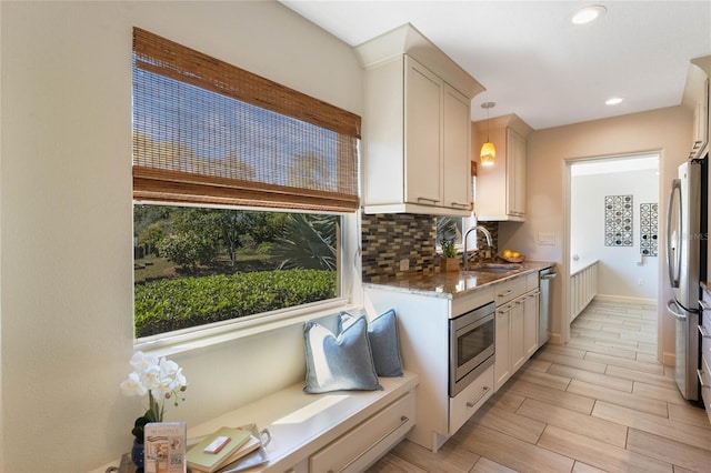 kitchen with wood finish floors, a sink, tasteful backsplash, appliances with stainless steel finishes, and hanging light fixtures