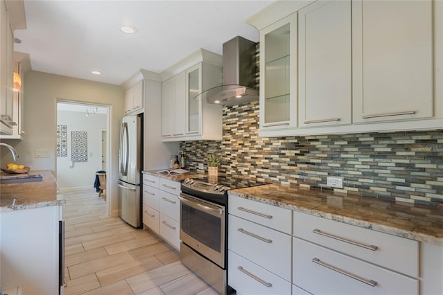 kitchen with wood finish floors, a sink, stainless steel appliances, wall chimney exhaust hood, and decorative backsplash