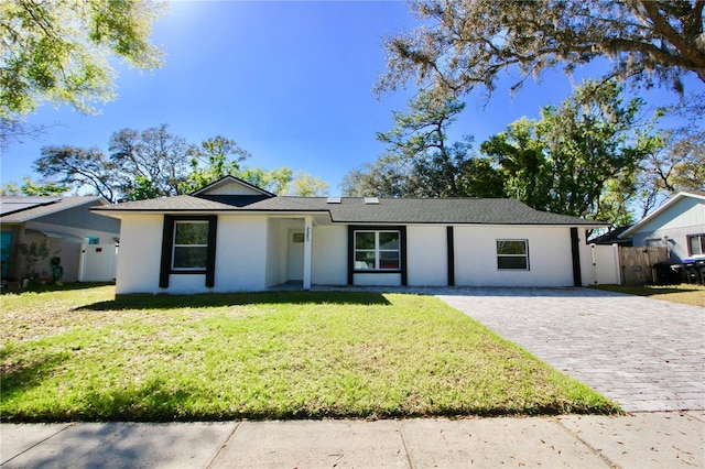 ranch-style home with a front lawn, decorative driveway, fence, and stucco siding