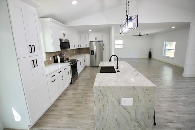 kitchen featuring lofted ceiling, a sink, stainless steel appliances, open floor plan, and backsplash