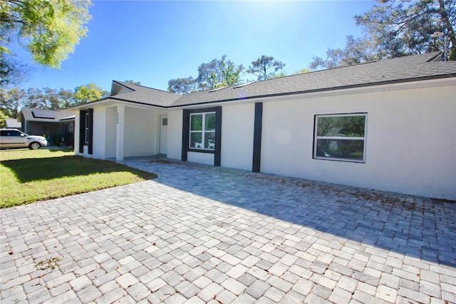 ranch-style home with a front lawn, roof with shingles, and stucco siding