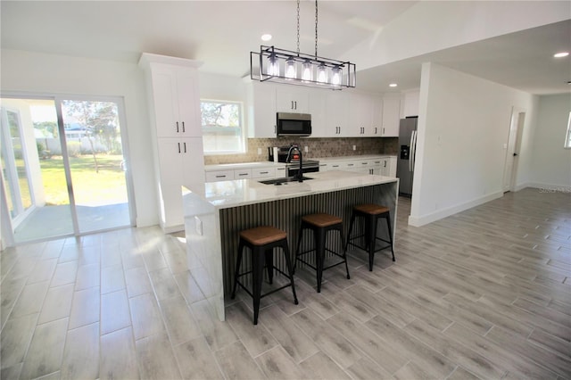 kitchen featuring a center island with sink, a breakfast bar, a sink, decorative backsplash, and stainless steel appliances