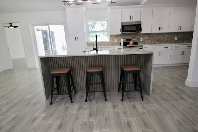 kitchen featuring a kitchen island with sink, a sink, decorative backsplash, stainless steel appliances, and white cabinets