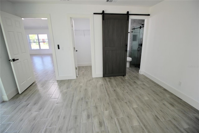 unfurnished bedroom featuring a spacious closet, baseboards, wood tiled floor, a barn door, and a closet