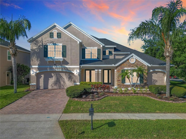 traditional home with a front yard, stucco siding, decorative driveway, stone siding, and an attached garage