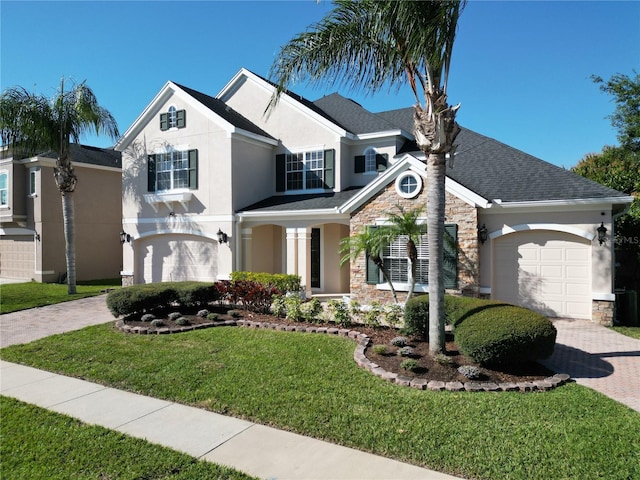 view of front facade featuring stucco siding, decorative driveway, stone siding, a front yard, and a garage