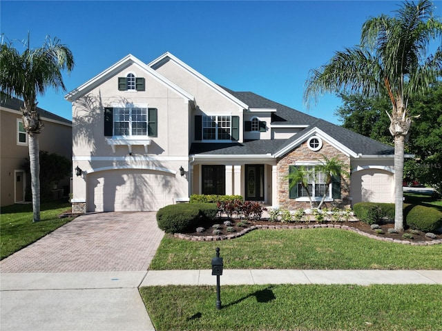 traditional home featuring decorative driveway, stone siding, an attached garage, and stucco siding