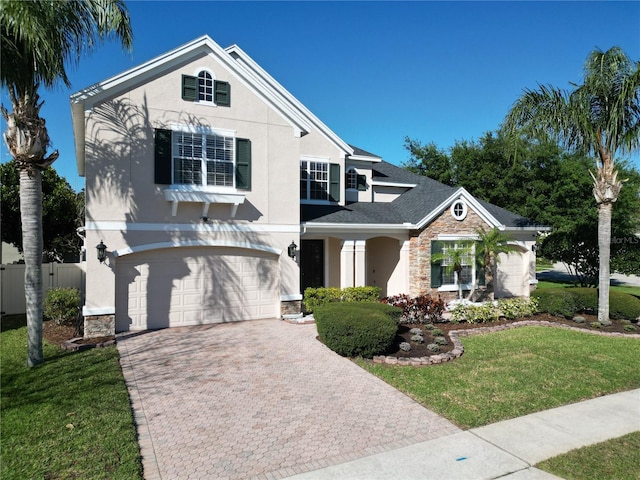 view of front of house with stucco siding, a front lawn, decorative driveway, stone siding, and a garage