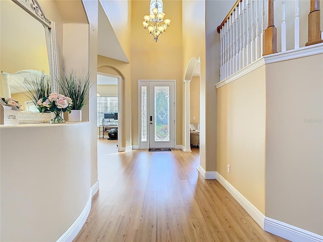 foyer entrance featuring wood finished floors, baseboards, a high ceiling, arched walkways, and a chandelier