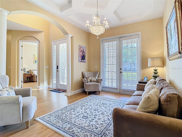 living area featuring coffered ceiling, arched walkways, light wood finished floors, baseboards, and ornate columns