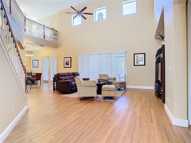 living room with stairway, baseboards, light wood-style floors, and ceiling fan with notable chandelier