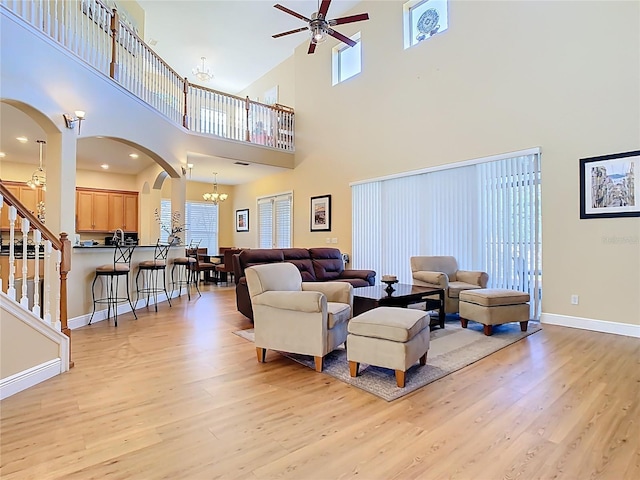 living room with light wood-type flooring, arched walkways, baseboards, and ceiling fan with notable chandelier