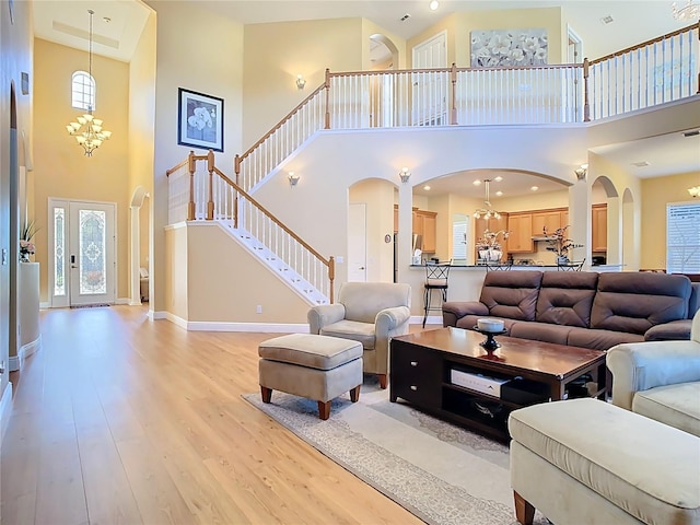 living room featuring light wood-type flooring, stairway, arched walkways, baseboards, and a chandelier