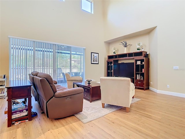 living area with a high ceiling, baseboards, and wood finished floors