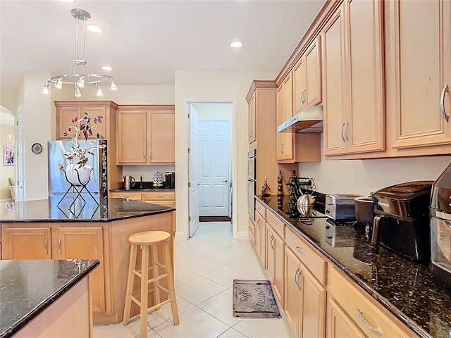 kitchen featuring under cabinet range hood, dark stone countertops, a kitchen island, freestanding refrigerator, and recessed lighting