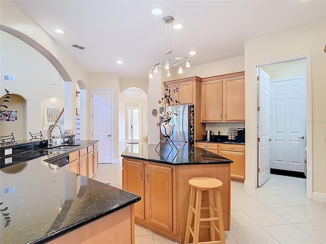 kitchen with visible vents, a kitchen island, freestanding refrigerator, arched walkways, and a sink