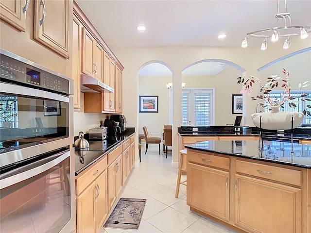 kitchen with double oven, light brown cabinets, arched walkways, and under cabinet range hood