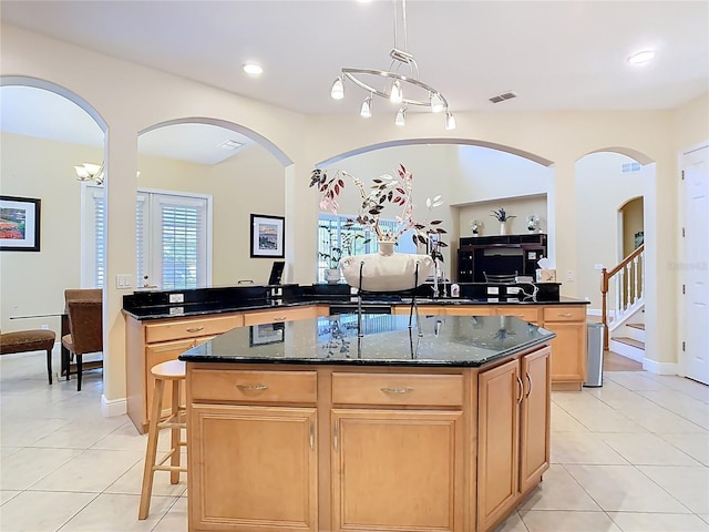 kitchen with dark stone countertops, light tile patterned floors, light brown cabinets, and a kitchen island