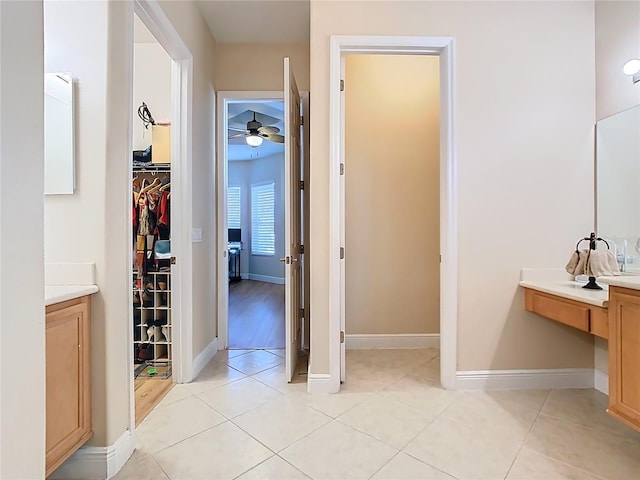 bathroom featuring a walk in closet, tile patterned flooring, baseboards, ceiling fan, and vanity