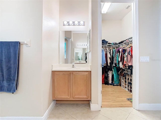 bathroom with a spacious closet, visible vents, baseboards, tile patterned floors, and vanity