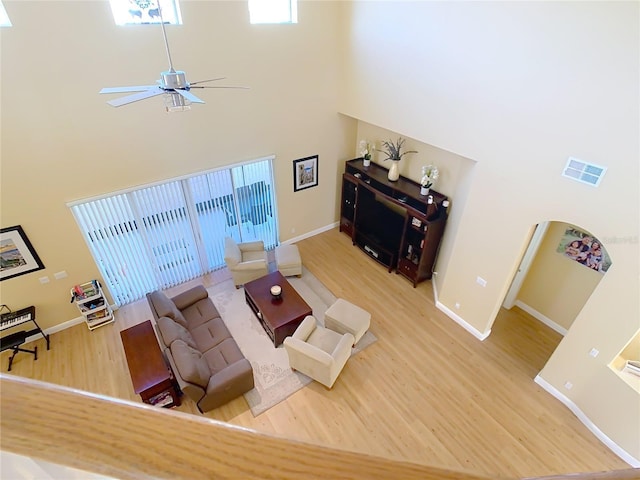 living room with visible vents, ceiling fan, baseboards, a towering ceiling, and wood finished floors