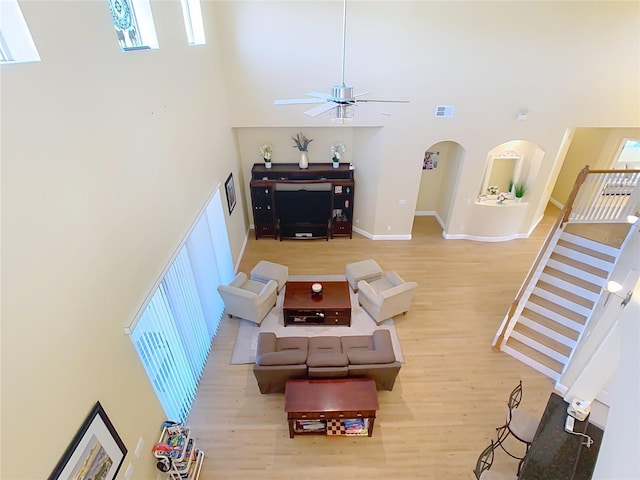 living area featuring arched walkways, visible vents, light wood-style flooring, and a towering ceiling