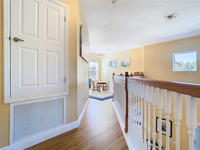 hallway with wood finished floors, a notable chandelier, an upstairs landing, and visible vents