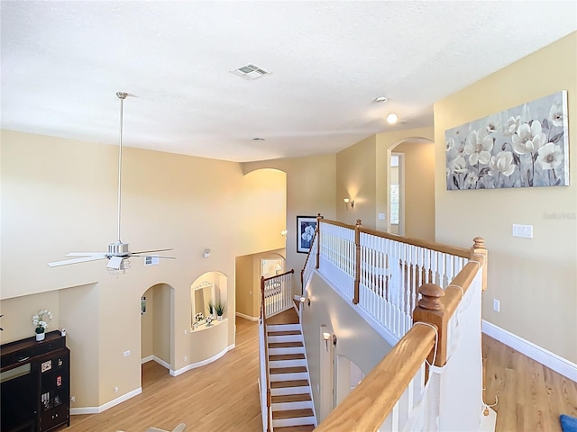 hall with visible vents, baseboards, arched walkways, light wood-style floors, and an upstairs landing