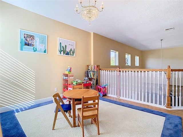 recreation room with wood finished floors, baseboards, visible vents, a textured ceiling, and a chandelier