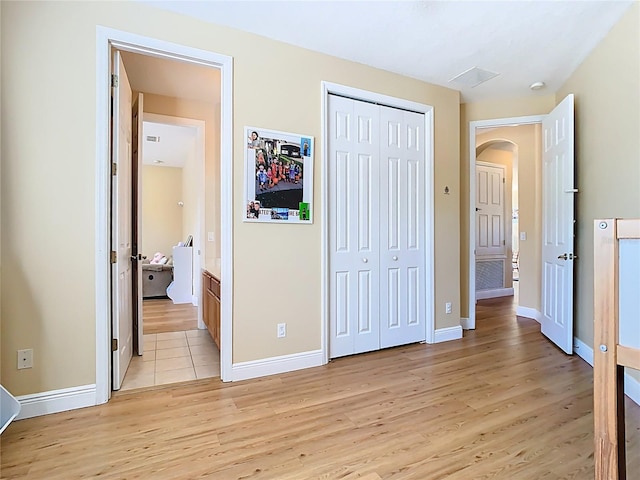 unfurnished bedroom featuring a closet, light wood-style flooring, arched walkways, and baseboards