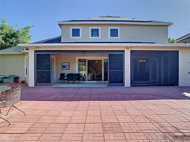 back of house featuring roof mounted solar panels, stucco siding, outdoor dining area, a sunroom, and a patio area